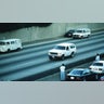 Motorists wave as police cars pursue the Ford Bronco driven by Al Cowlings, carrying fugitive murder suspect O.J. Simpson